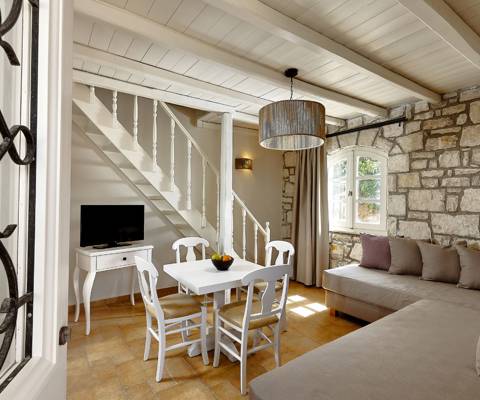 Marni Hotel House Maisonette living room with stone wall, staircase, dining table, corner sofa and TV