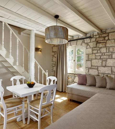Marni Hotel House Maisonette living room with stone wall, staircase, dining table, corner sofa and TV