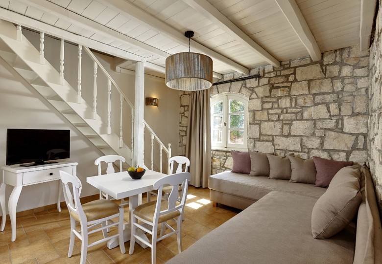Marni Hotel House Maisonette living room with stone wall, staircase, dining table, corner sofa and TV